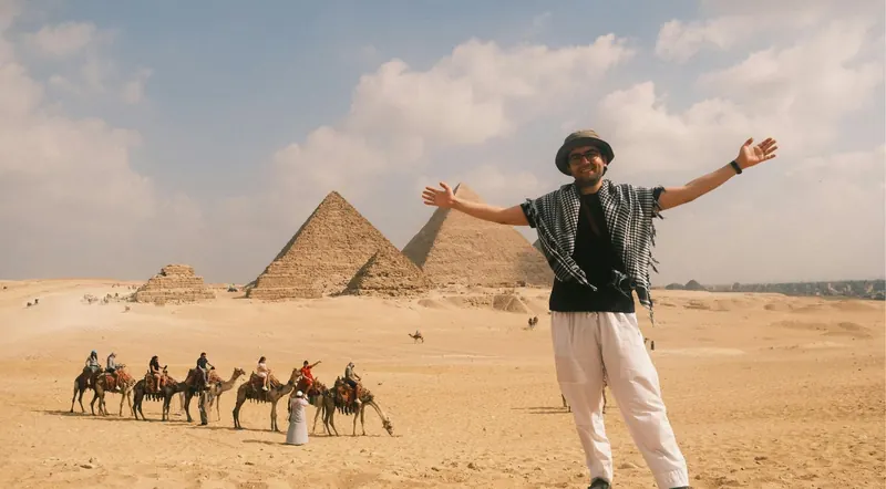 A happy traveler with arms raised in front of the Giza pyramids